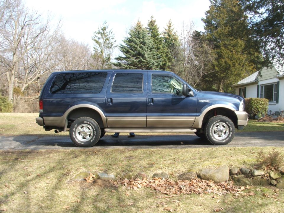 Dark blue and tan Ford Excursion SUV, side view, parked on a driveway