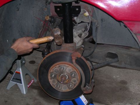 1992 Ford Taurus - A mechanic works on the suspension of a vehicle, using a hammer on a suspension component.