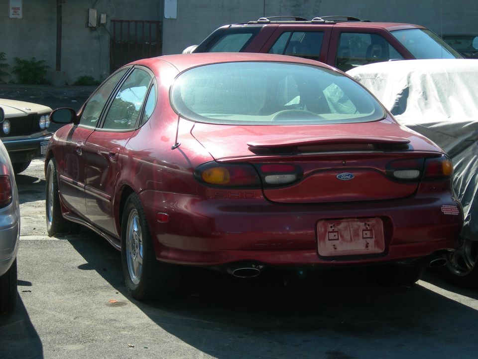 Rear view of a red Ford Taurus sedan parked next to other vehicles