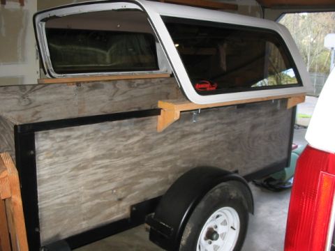 1995 Ford Bronco - A trailer is fitted with a white camper shell, resting on wooden supports.