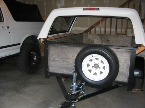 1995 Ford Bronco - A white 1995 Ford Bronco is seen parked next to a custom-built trailer, complete with a spare tire mounted on the side.