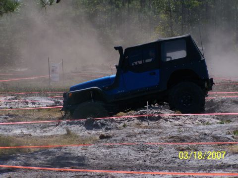 1989 Ford Bronco - A blue Jeep Wrangler tackles an off-road obstacle course on a dusty day.