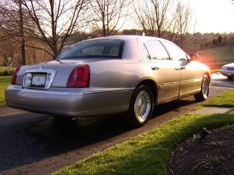 1996 Mercury Grand Marquis - Rear view of a tan sedan with distinctive chrome trim and red taillights, parked outdoors during golden hour.