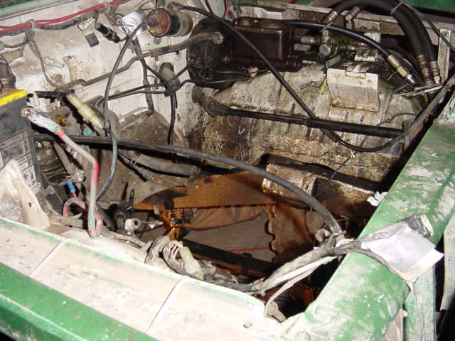 Engine bay of green truck stripped down, transmission tunnel and wiring exposed, battery cable visible