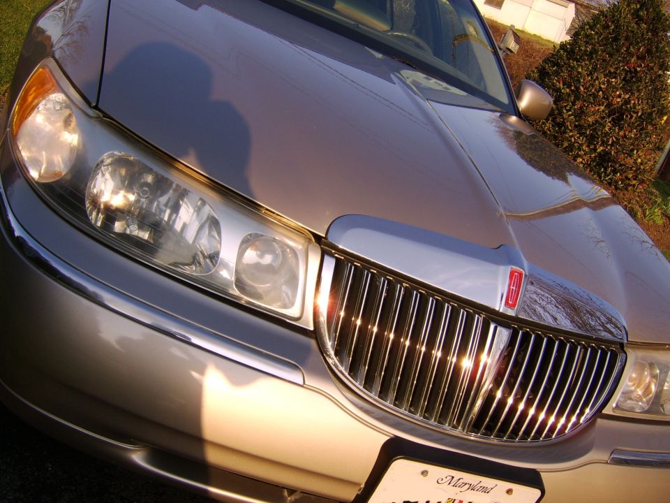 Close-up of a champagne-gold sedan's chrome Lincoln-style waterfall grille and headlights, Maryland plate below