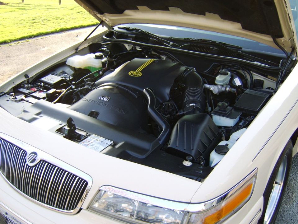 Open engine bay of white Mercury Grand Marquis showing black V8 cover and reservoirs