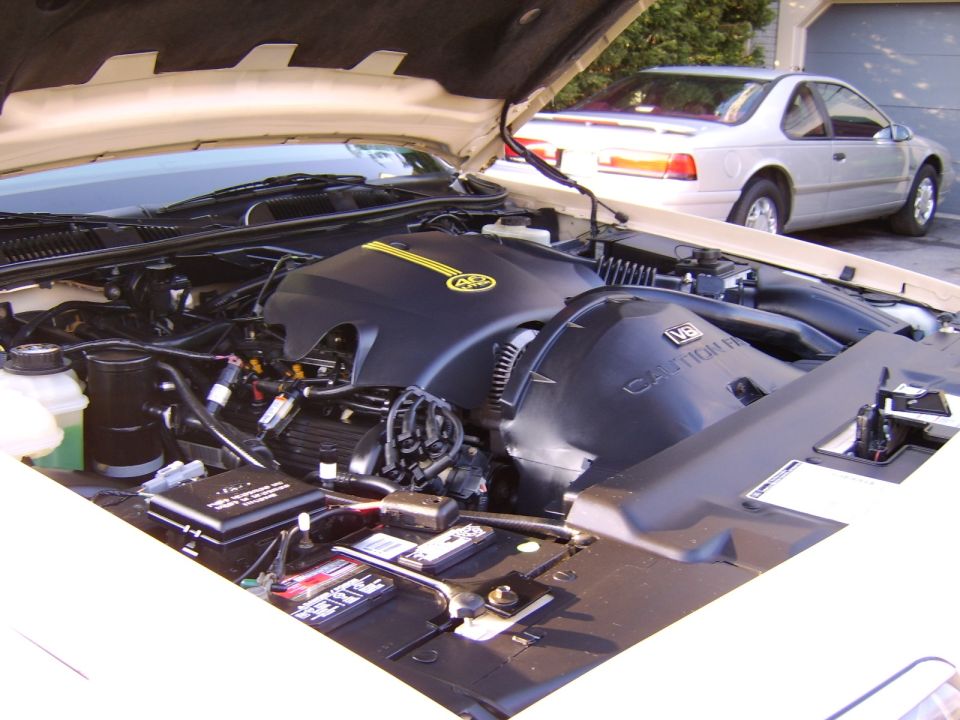 Open engine bay showing black V8 engine cover, battery and wiring, hood up