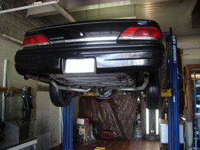 1992 Ford Crown Victoria - The rear of a black Ford Crown Victoria is shown elevated on a car lift for maintenance.