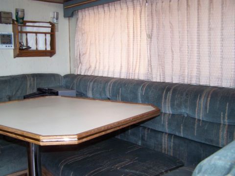 1989 Ford F-250 - The interior of a camper van shows a dinette area with upholstered seating and a table, alongside a digital clock mounted on the wall.