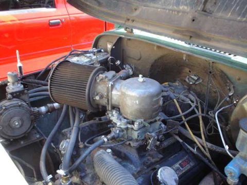 1973 Ford F-100 - Close-up of an open engine bay showing a V-engine with a conical air filter, a large cylindrical vacuum/converter canister, and a carbureto…