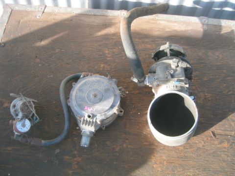 1973 Ford F-100 - Three disassembled propane/LPG fuel system components laid on a weathered plywood surface, including what appears to be an Impco carburetor…