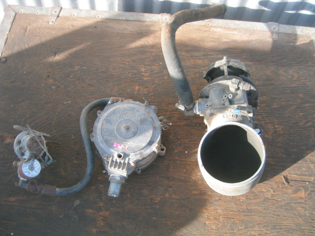 Disassembled propane fuel system parts including mixer, regulator, and air horn on plywood.