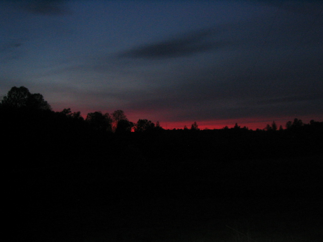Dark sky with a red sunset horizon over silhouetted trees and a dark foreground. "SUPERMOTORS" text is visible