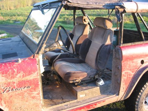 1968 Ford Bronco - The interior of a red Ford Bronco shows its worn seats, roll cage, and missing doors.