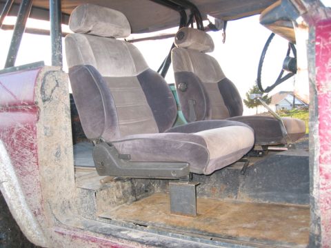 1968 Ford Bronco - The interior of a vehicle shows fabric seats, a roll cage, and a steering wheel, with mud on the door panel.
