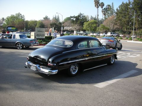 1998 Ford Crown Victoria - glossy black lowered and chopped vintage Mercury custom sedan with whitewall-style wheels driving along a street near a Subway sign.