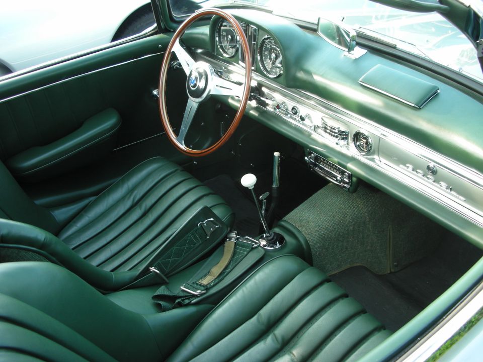 Classic roadster interior with dark green leather seats, wood-rim wheel and floor shifter