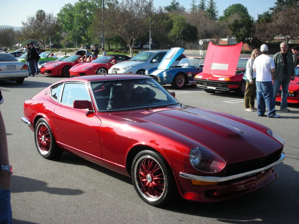 Dark red Datsun 240Z-style classic coupe on custom red wheels at a car meet
