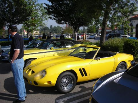 1998 Ford Crown Victoria - bright yellow open-top classic Ferrari-style sports car on chrome wire wheels parked at a car show as a man looks on.