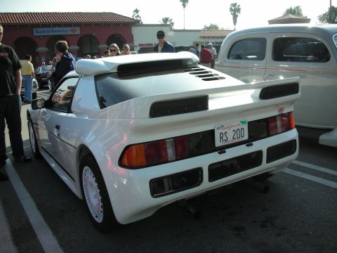 1998 Ford Crown Victoria - Rear three-quarter of a white mid-engine sports car with a tall rear wing and a California 'RS 200' license plate in a parking lot.