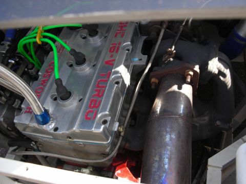 1998 Ford Crown Victoria - Close-up of an engine bay with a cam cover reading 'Cosworth DOHC 16-V Turbo' alongside green plug wires and exhaust piping.