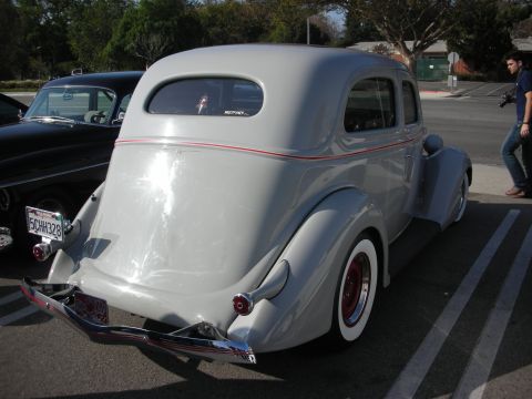 1998 Ford Crown Victoria - Rear three-quarter of a gray 1930s-style two-door sedan hot rod with red wire wheels and wide whitewall tires at a car show.