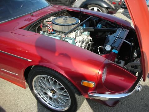 1998 Ford Crown Victoria - maroon Datsun sports car with its hood open reveals a V8 swap with chrome air cleaner; the fender wears multi-spoke wheels.