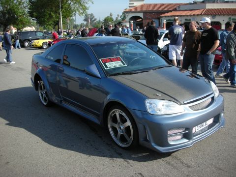 1998 Ford Crown Victoria - gray Honda Civic coupe fitted with a wide body kit and a For Sale sign sits among a crowd at an outdoor car meet.