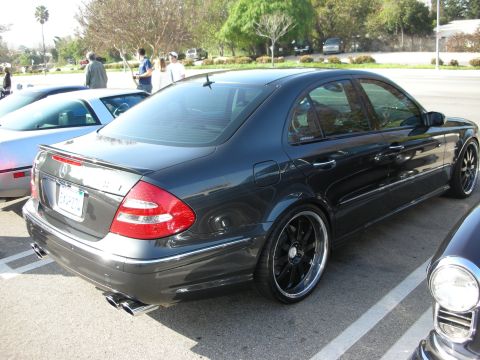 1998 Ford Crown Victoria - Rear three-quarter of a dark gray Mercedes-Benz E-Class sedan, lowered on black multi-spoke wheels with dual exhaust, in a lot.