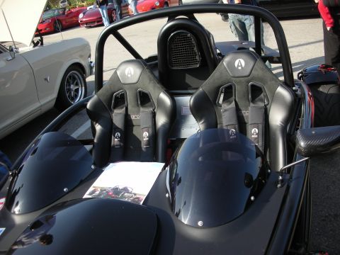 1998 Ford Crown Victoria - Two black Sparco bucket seats with Ariel-badged headrests sit in an open tube-frame car, a white classic coupe parked behind.