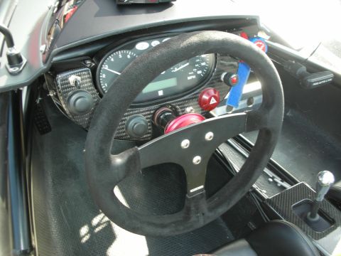 1998 Ford Crown Victoria - Stripped race-car interior showing a black suede steering wheel, carbon-fiber dashboard and a central analog speedometer with toggle switch…