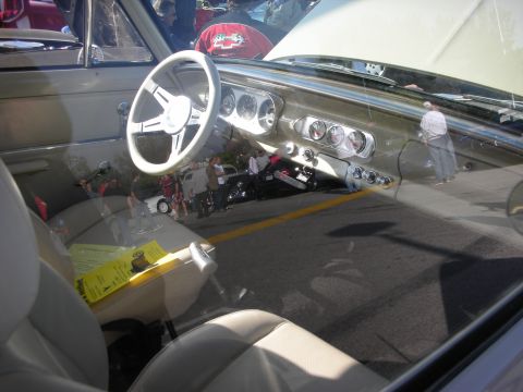 1998 Ford Crown Victoria - View through a windshield into a vintage car's tan interior, showing a white steering wheel, round gauges and a paper show card on the seat.
