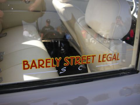 1998 Ford Crown Victoria - car's side window bears a red and yellow BARELY STREET LEGAL decal, with a tan leather interior visible behind it.