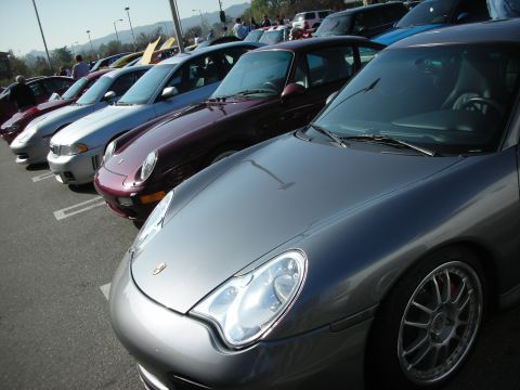 1998 Ford Crown Victoria - row of parked sports cars angles into the distance, led by a silver Porsche 911 with its crest visible on the hood.