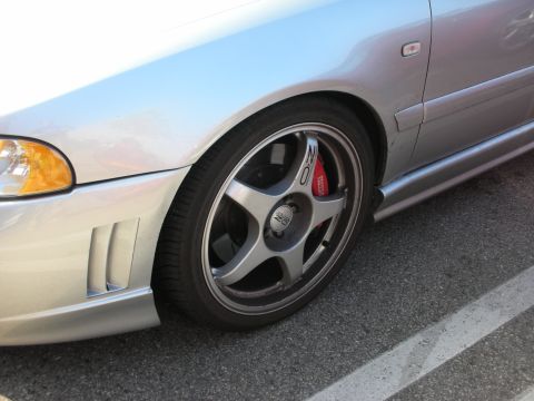 1998 Ford Crown Victoria - Close-up of a silver sedan's front corner showing a gray five-spoke wheel and red brake caliper over a slotted rotor.