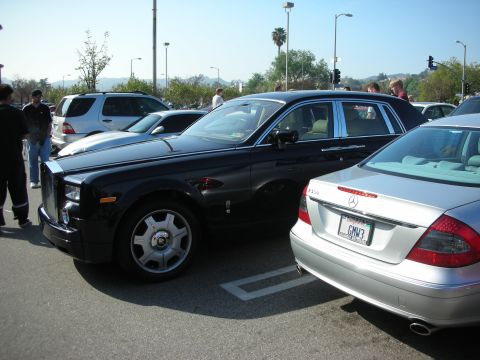 1998 Ford Crown Victoria - black Rolls-Royce Phantom sits beside a silver Mercedes coupe with plate GMN3 in a crowded show parking lot.