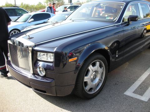 1998 Ford Crown Victoria - Front three-quarter of a dark purple Rolls-Royce Phantom showing its chrome grille, round headlamp and alloy wheel.