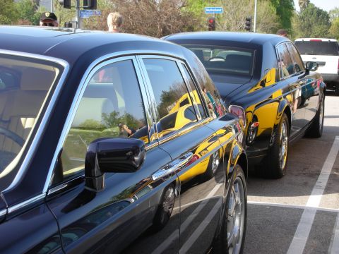 1998 Ford Crown Victoria - Two black Rolls-Royce Phantom sedans parked nose to tail, their glossy panels reflecting nearby cars at an outdoor meet.