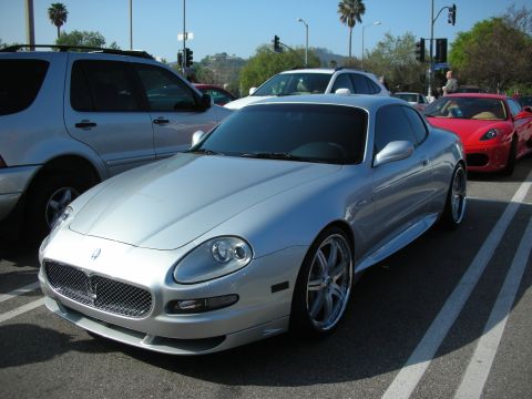 1998 Ford Crown Victoria - silver Maserati coupe with mesh grille and multi-spoke wheels parked on a street with a red Ferrari visible behind.