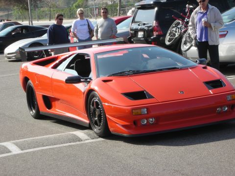1998 Ford Crown Victoria - orange Lamborghini Diablo with a large rear wing sits in a lot while people and a bike-rack SUV stand nearby.