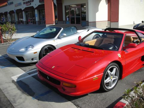 1998 Ford Crown Victoria - red Ferrari F355 Spider parks beside a silver Ferrari 360 Spider in front of storefronts.