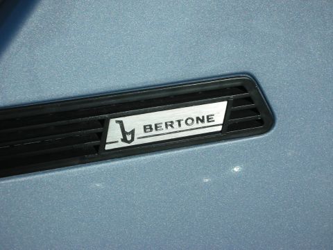 1998 Ford Crown Victoria - Close-up of a Bertone emblem mounted on a louvered vent panel of light-blue bodywork.