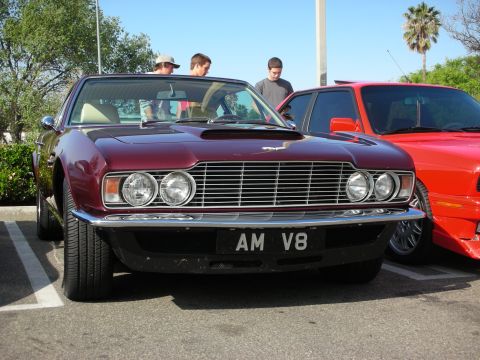 1998 Ford Crown Victoria - Front view of a maroon Aston Martin DBS V8 with quad headlights and AM V8 plate, spectators standing behind it.