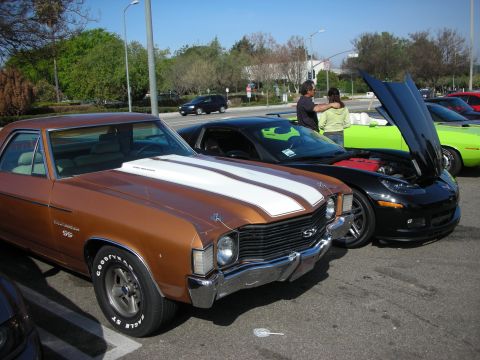 1998 Ford Crown Victoria - brown Chevrolet El Camino SS with white stripes parks beside a black Corvette and green muscle car at a meet.
