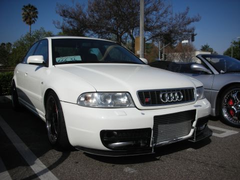 1998 Ford Crown Victoria - white Audi S4 sedan with black wheels and an added front splitter sits in a lot beside a silver coupe.
