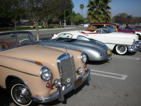 1998 Ford Crown Victoria - row of vintage convertibles lines a lot, led by a tan Mercedes-Benz, a silver Porsche-style speedster and a white Cadillac.