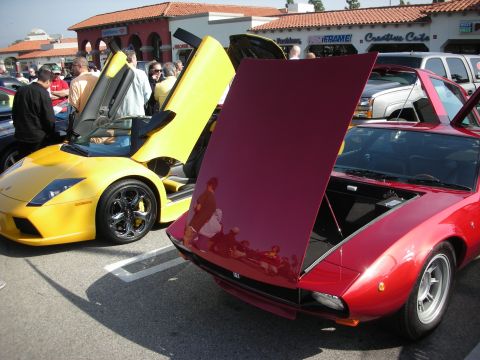 1998 Ford Crown Victoria - yellow Lamborghini with one scissor door raised is parked next to a maroon coupe whose hood is propped open at a car show.