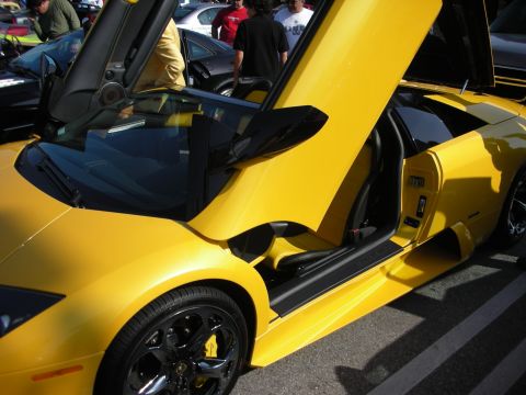 1998 Ford Crown Victoria - yellow Lamborghini Murcielago is shown side-on with its scissor door raised and black alloy wheels at a car gathering.