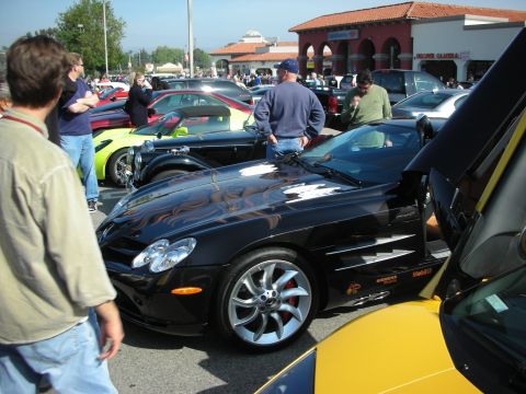 1998 Ford Crown Victoria - black Mercedes-Benz SLR McLaren with its door raised draws onlookers in a packed shopping-center car show.