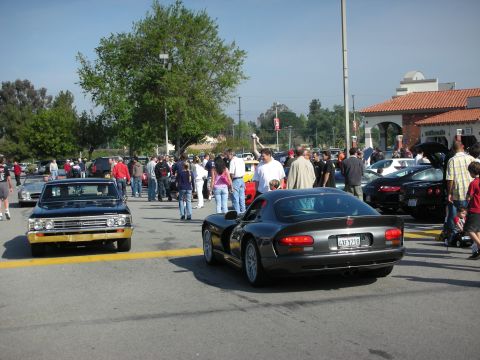 1998 Ford Crown Victoria - black Dodge Viper coupe and a black classic muscle car sit among a large crowd at a strip-mall car show.